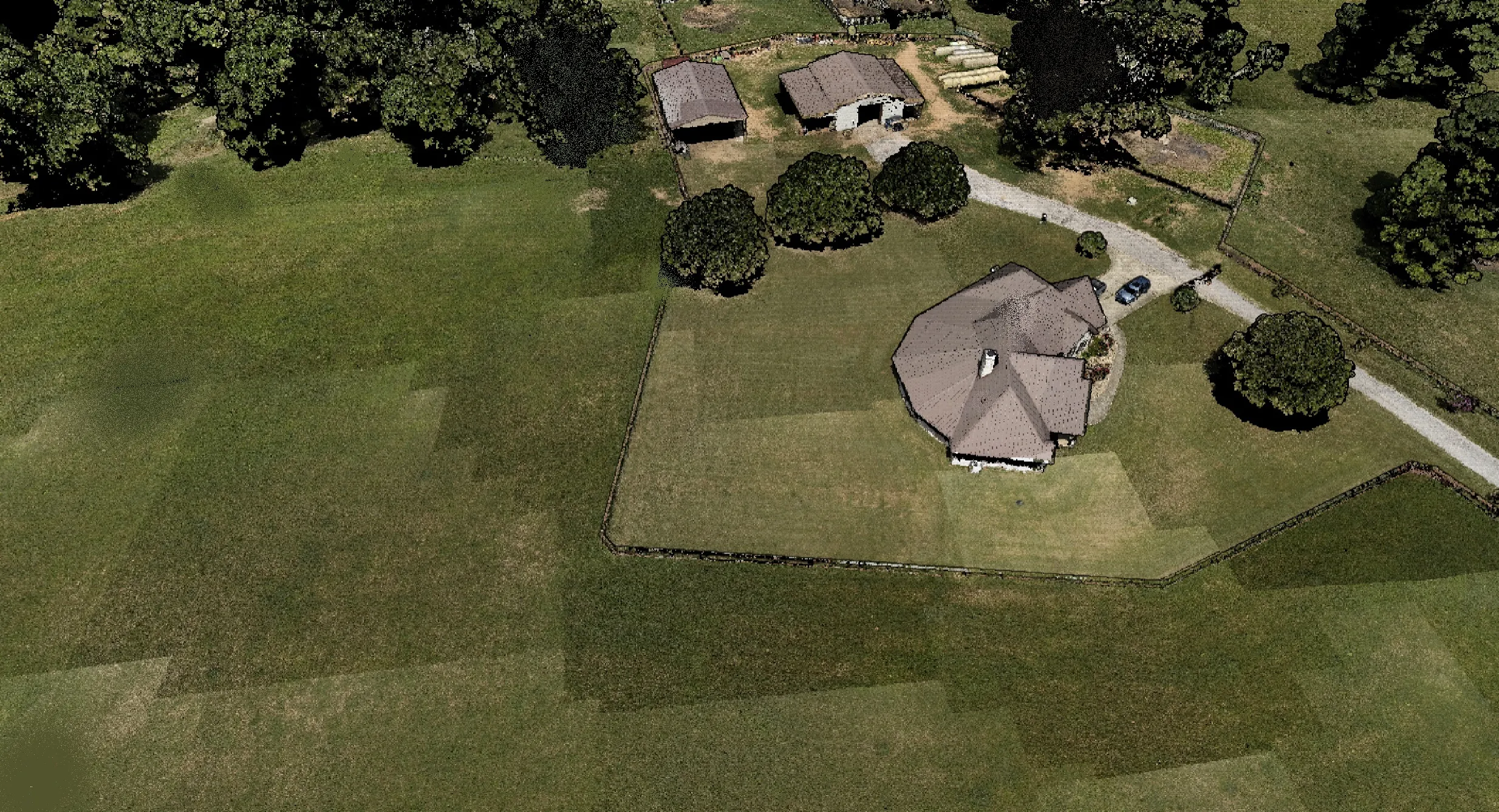 Aerial 3D reality-capture model of a residential property showing the house, outbuildings, driveway, and surrounding acreage